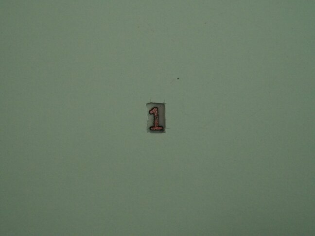 A hole in card-stock with the view of a cutout of the number 1 from the
plastic stencil.