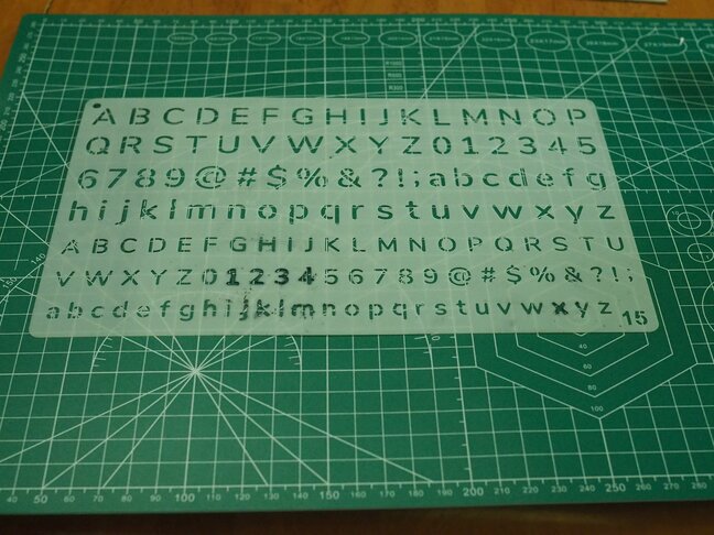 A plastic stencil of small letters, numbers, and symbols.